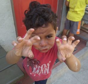 A boy with hands up and fingers curled makes a face like he is growling or roaring